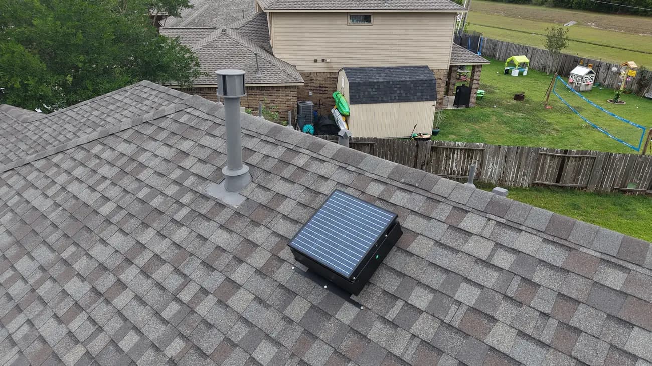 Aerial view of a solar attic fan and a vent stack on a residential roof
